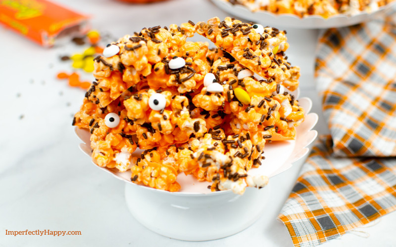 Halloween Popcorn from the Instant Pot sits on a white dish with fall colored napkin to the side. Spilled Reese's Pieces in the background.