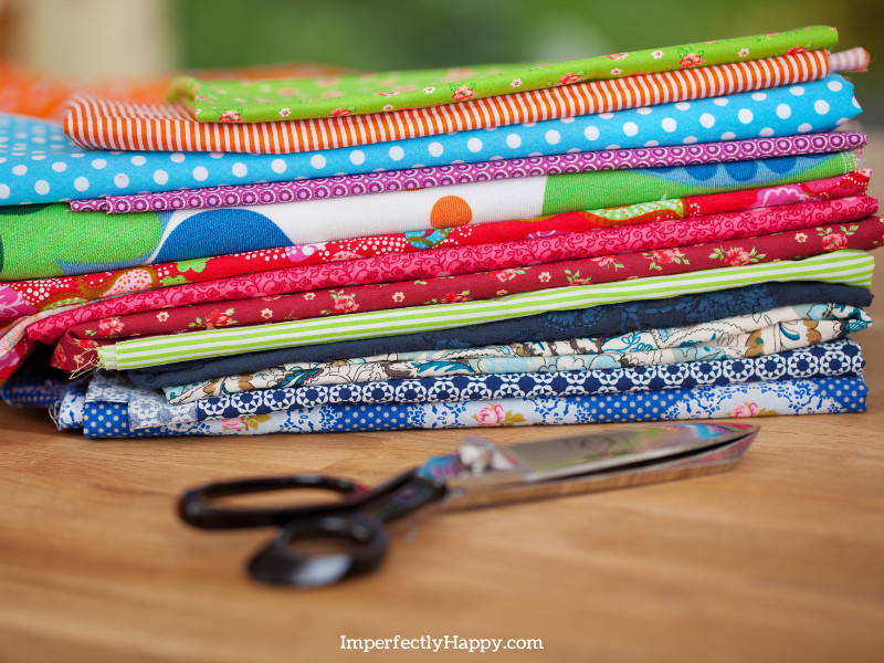 brightly colored fabrics folded on a table with sewing scissors