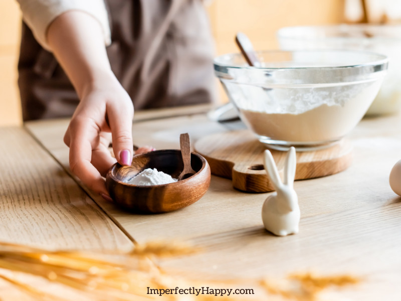 Baking ingredients on wooden table. Woman holding a bowl of baking powder.