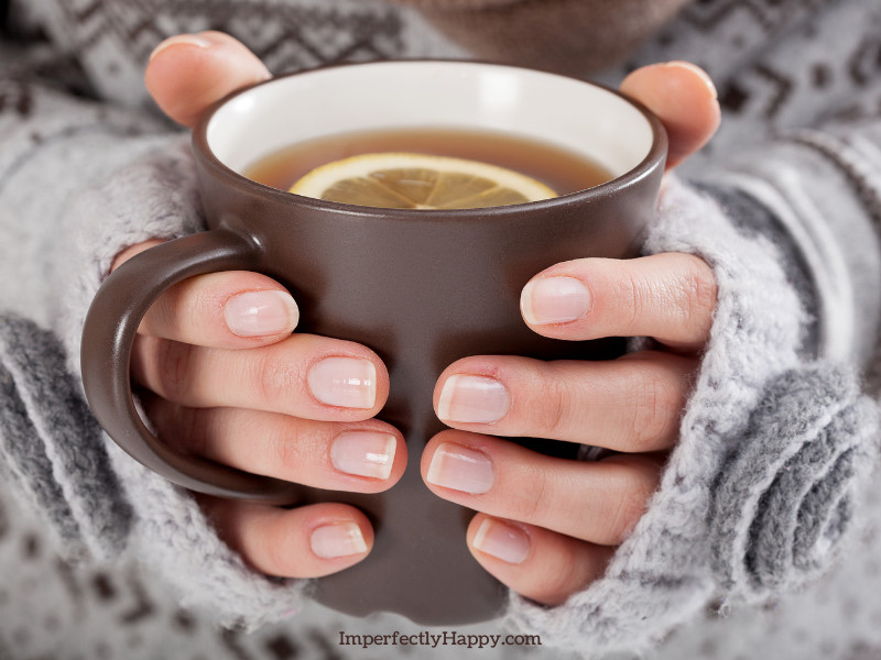 Home remedies for a sore throat - woman's hands hold a mug of tea.