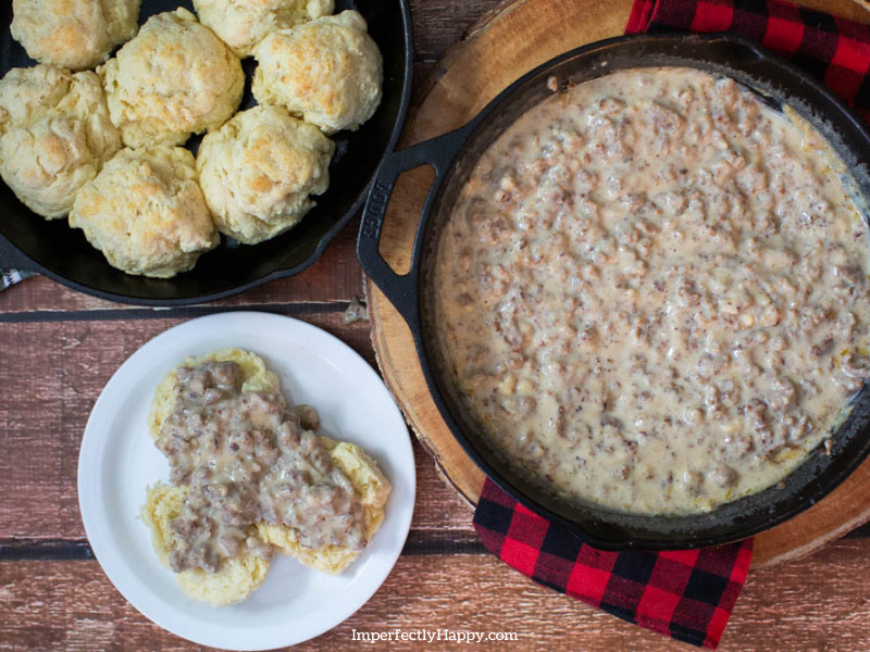 Sausage Gravy Recipe showing gravy in cast iron skillet with plat of biscuits with gravy on top.
